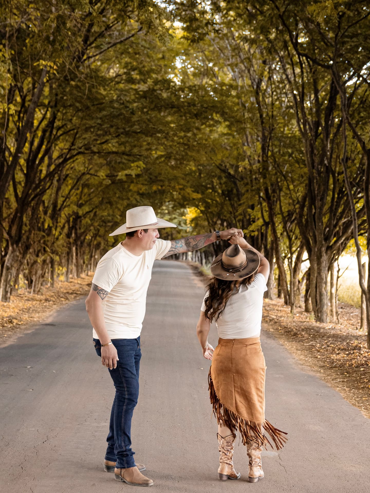 Casal country dançando em estrada arborizada ao entardecer