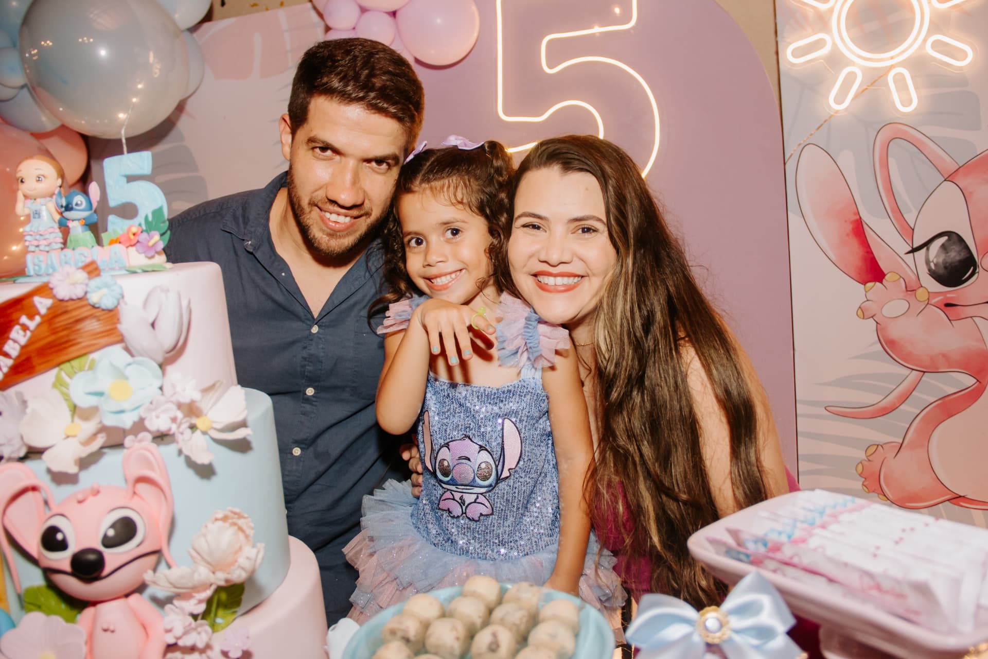 Pais e aniversariante sorrindo diante do bolo em festa temática