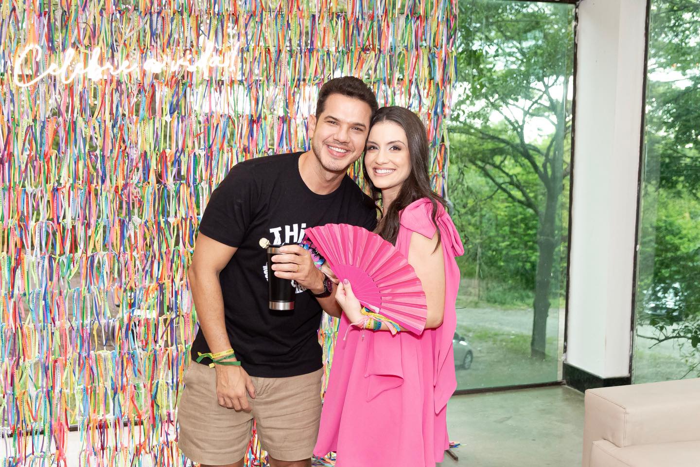 Casal aniversariante abraçado diante do painel de fitas coloridas