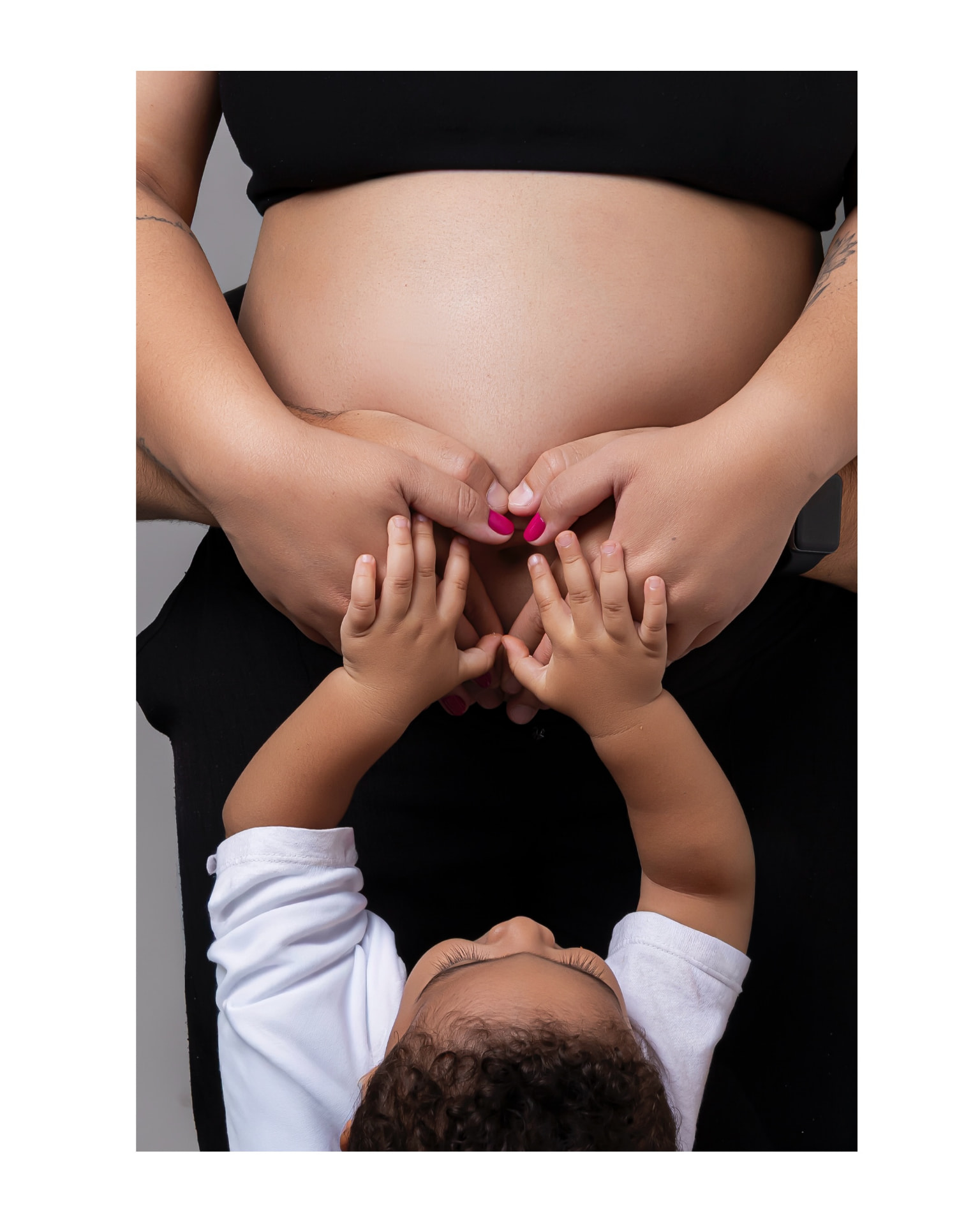 Mãos da mãe e do filho formando coração sobre a barriga