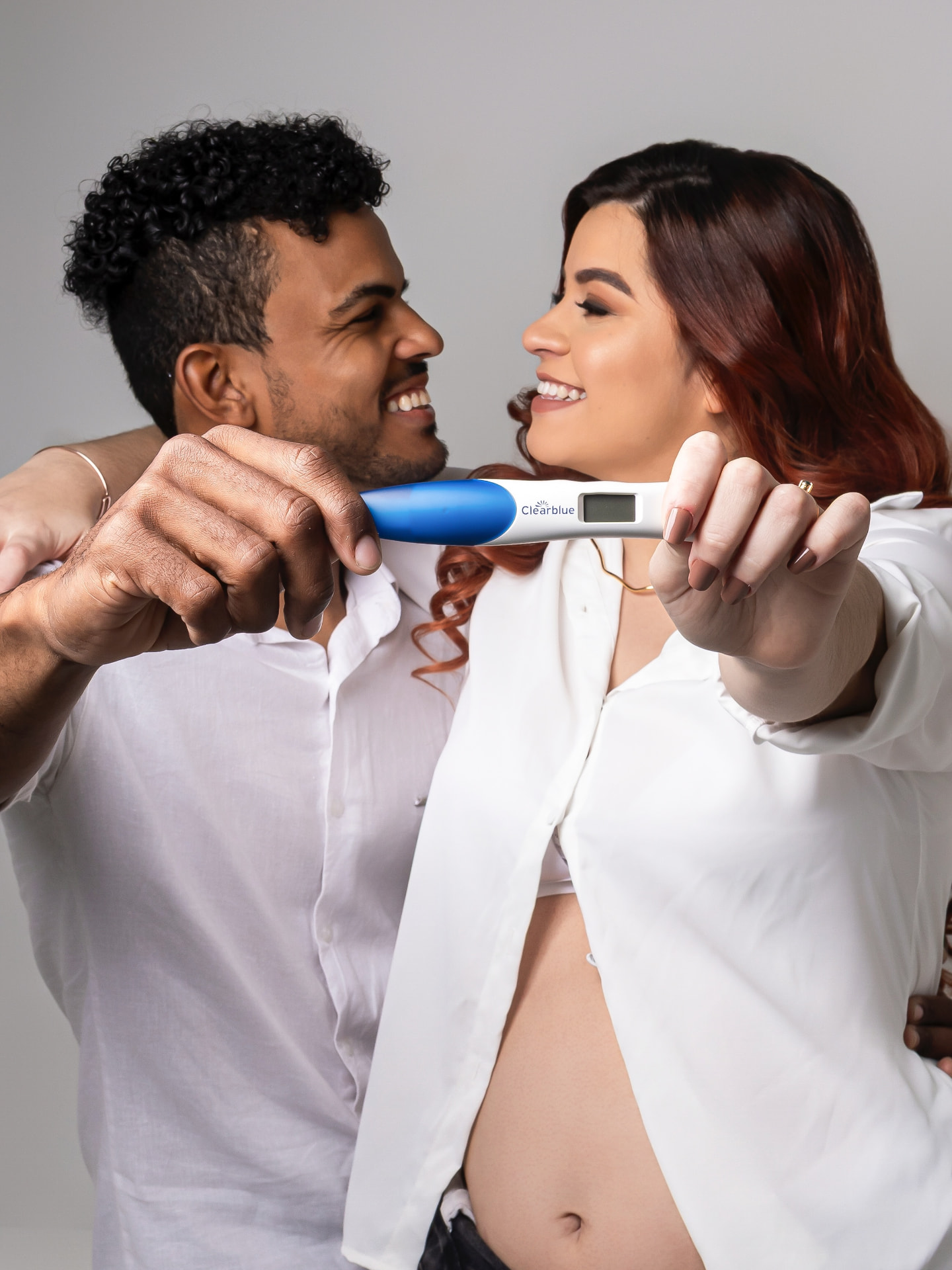 Casal sorrindo ao mostrar o teste de gravidez em ensaio de estúdio