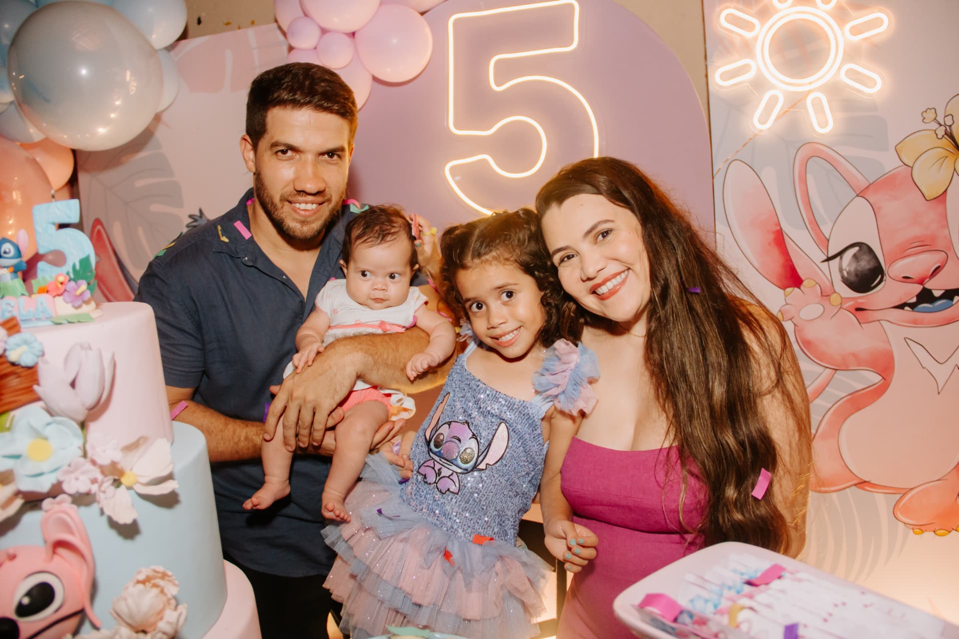 Família reunida com as filhas na mesa do bolo em festa de 5 anos