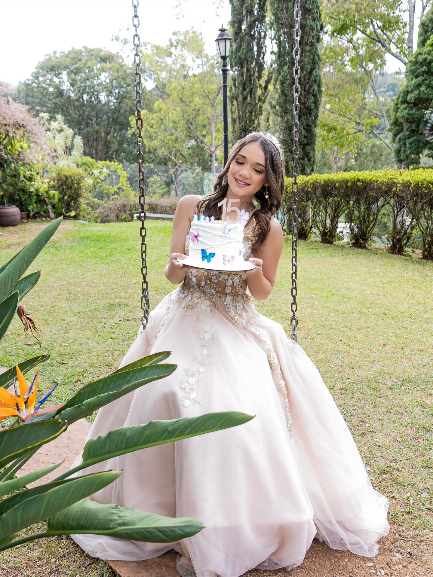 Debutante segurando o bolo decorado com borboletas em balanço no jardim